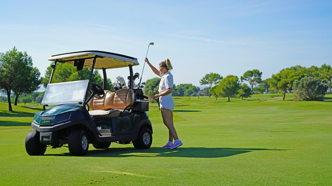 A golfer beside her golf cart on a sunny course