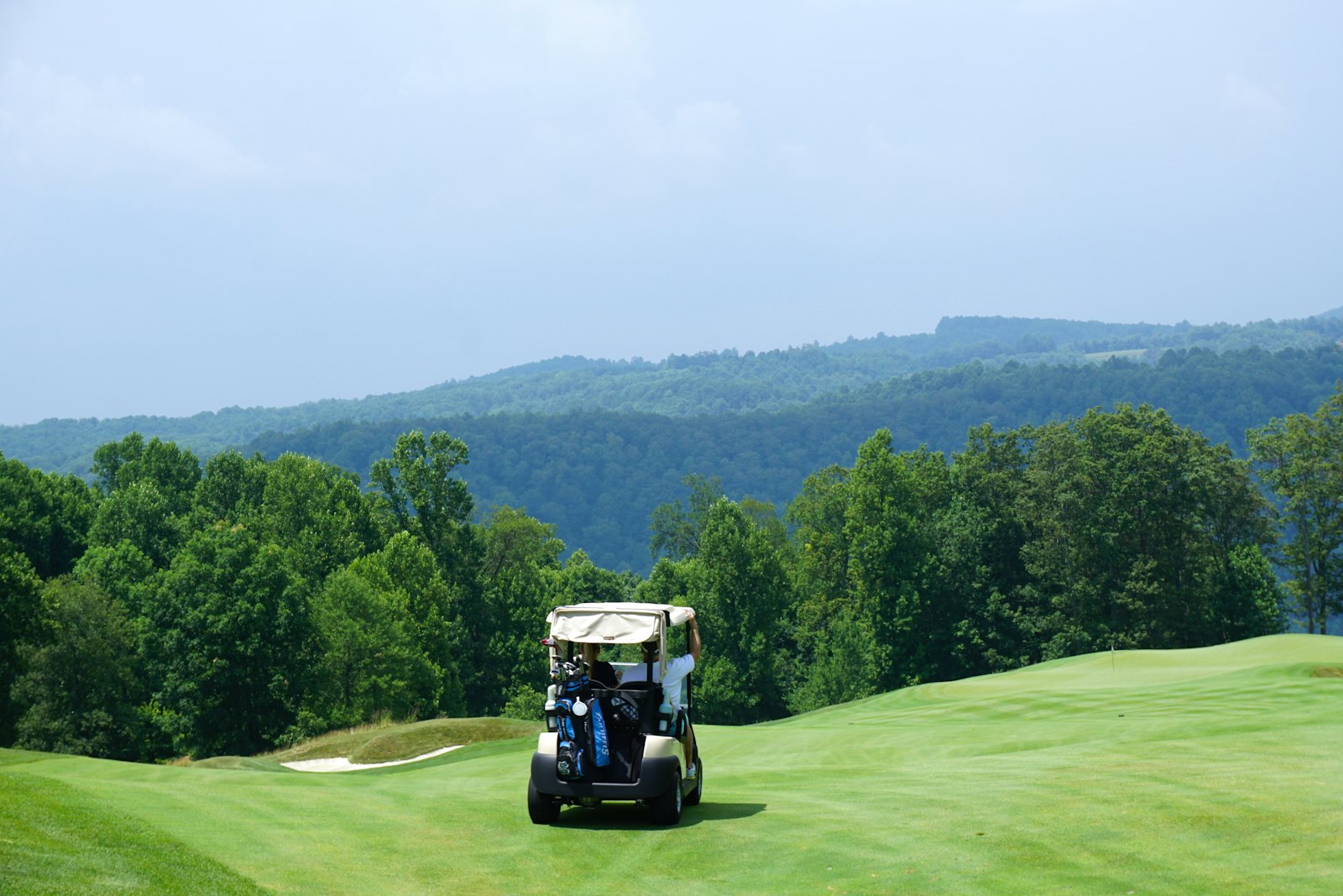 A golf cart on a hilltop fairway with mountains beyond